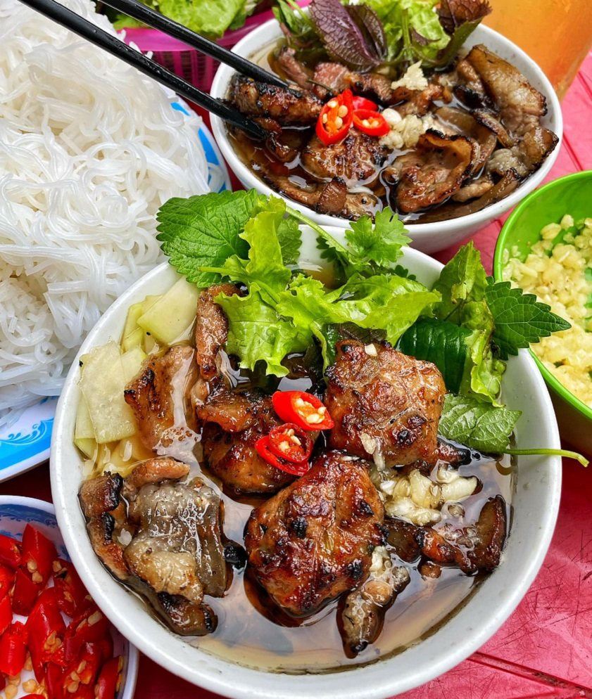 Bowls of bun cha with grilled pork, herbs and chopsticks on a Hanoi street table