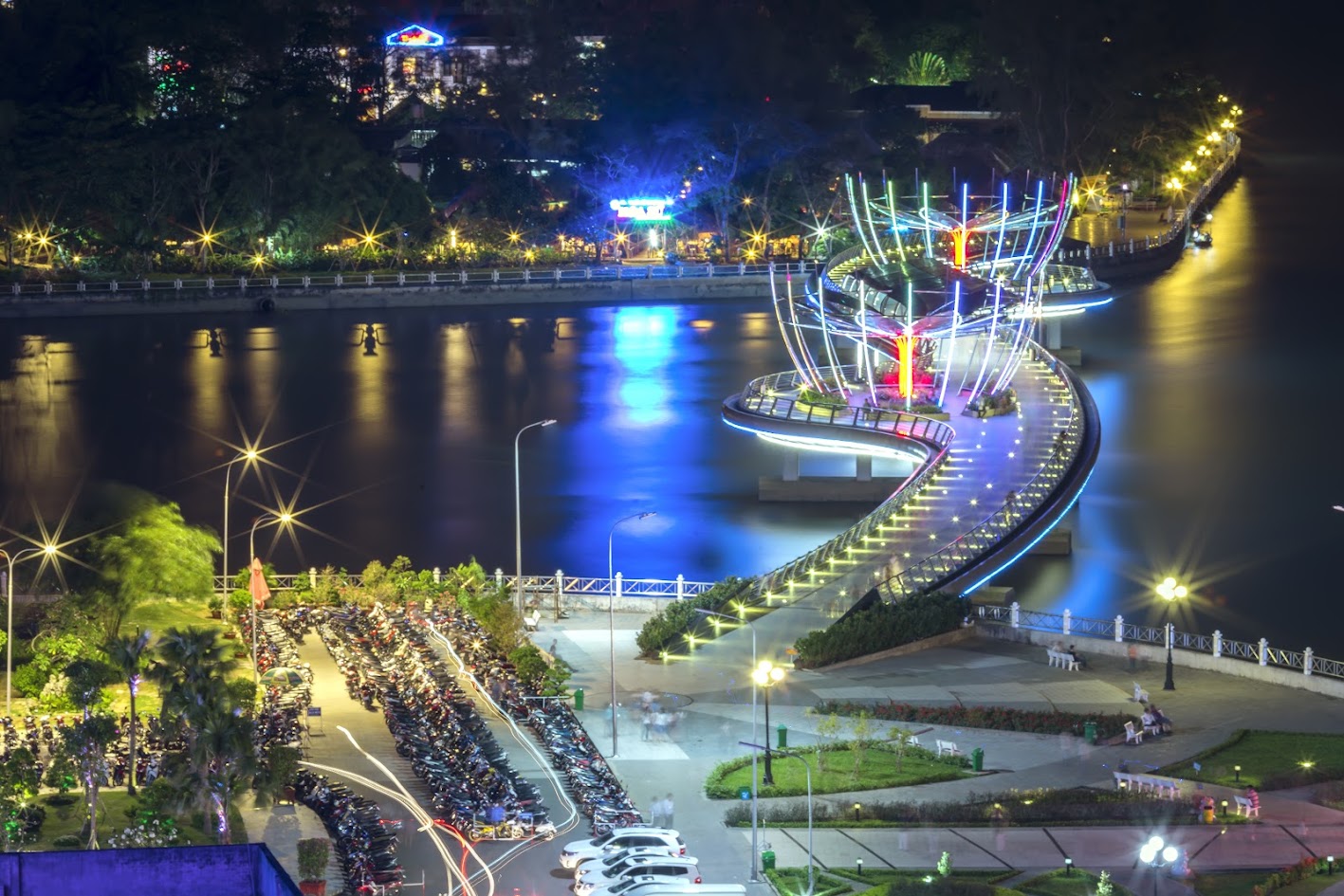 A riverside promenade in Can Tho lit up in the evening with boats on the water