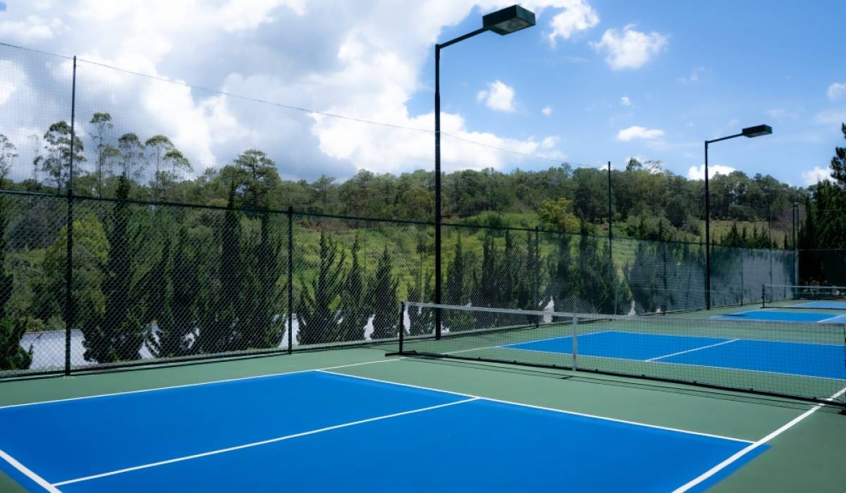 Blue pickleball courts in Da Lat surrounded by fencing, floodlights and pine-covered hills