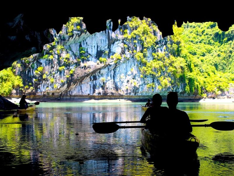 Kayakers paddling through the arch of Luon Cave in Ha Long Bay