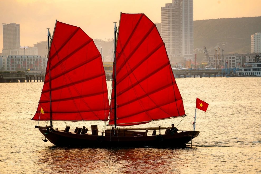 A traditional junk-style cruise boat sailing at sunset in Ha Long Bay