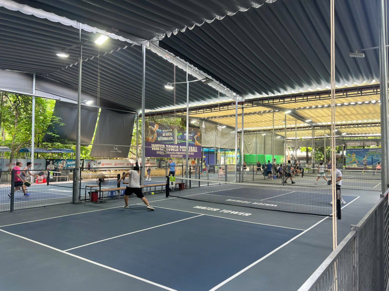 Covered pickleball courts in Hanoi with players at several nets under a metal roof