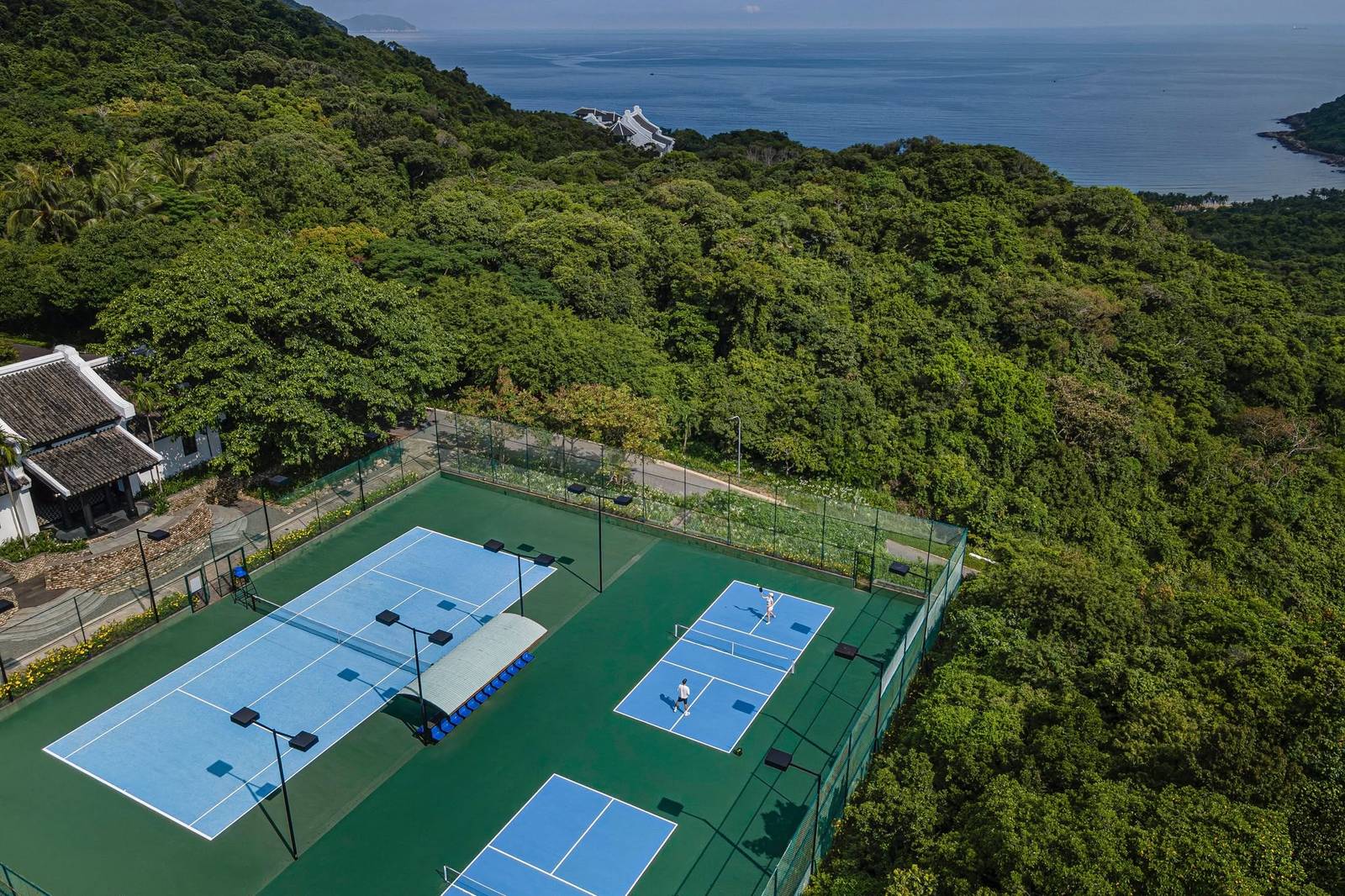 Aerial view of resort pickleball courts in the rainforest on the Son Tra peninsula, Da Nang, with the sea behind