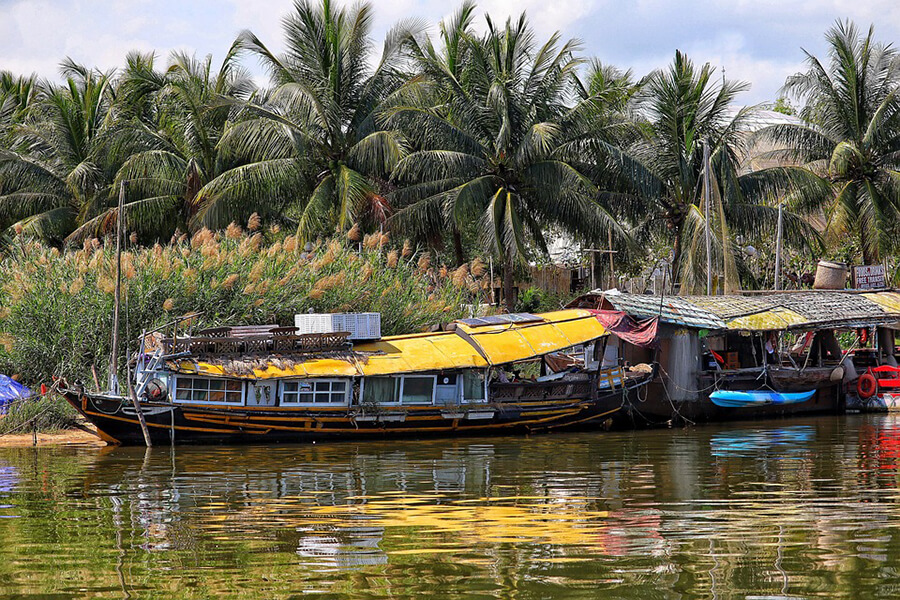 A wooden tour boat crossing a wide brown stretch of the Mekong River