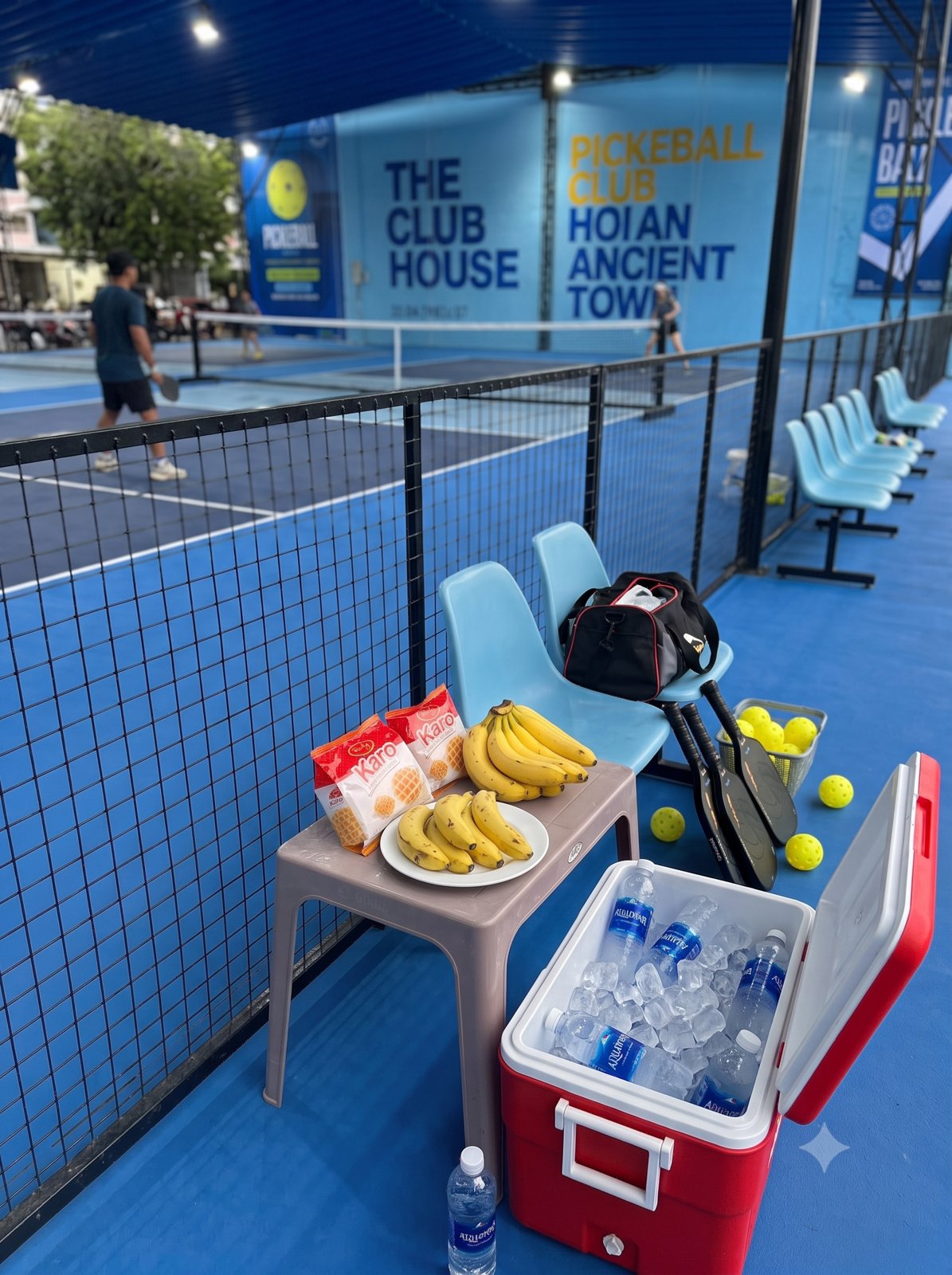 Snacks and drinks laid out on a bench beside a pickleball court in Vietnam