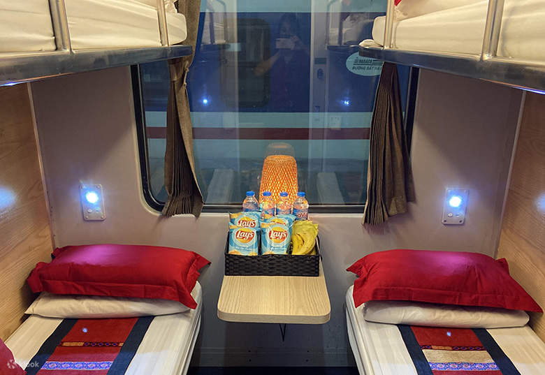 A neatly made lower bunk on a sleeper train with white pillows and a folded blanket