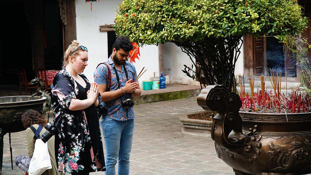 Visitors in modest clothing walking through the courtyard of a Vietnamese pagoda