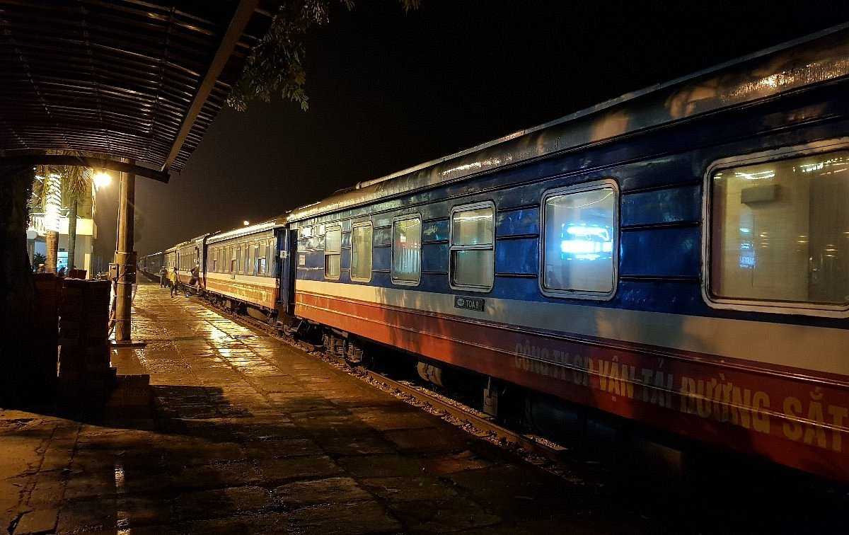 A long passenger train waiting at a station platform at night