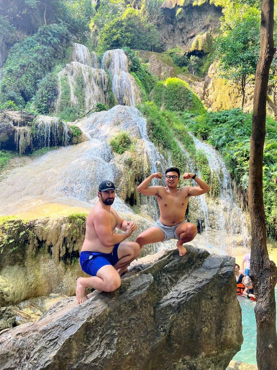 Travellers jumping off a cliff into a waterfall pool