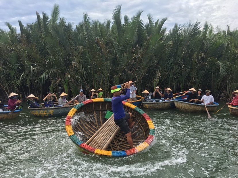 A local boatman spinning a round basket boat through the coconut forest near Hoi An