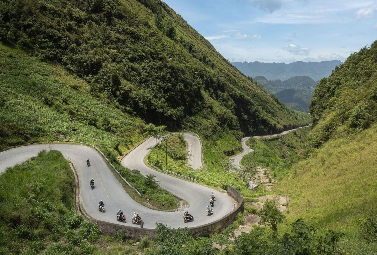 Switchback mountain road on the Ha Giang Loop with motorbikes and green valleys
