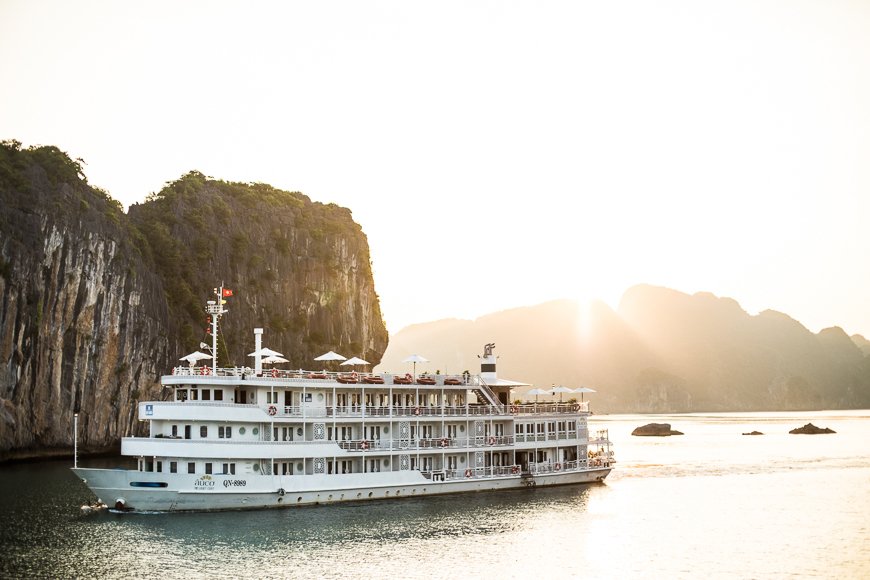 The Au Co cruise ship sailing past limestone karsts in Ha Long Bay at sunset